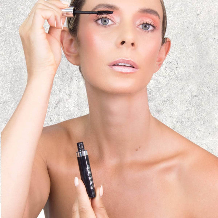 Woman applying mascara to her lashes against a neutral background